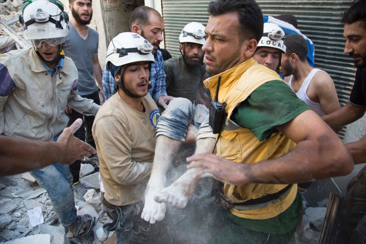 Syrian civil defense volunteers, known as the White Helmets, carry a body after digging it out from under the rubble of a bui