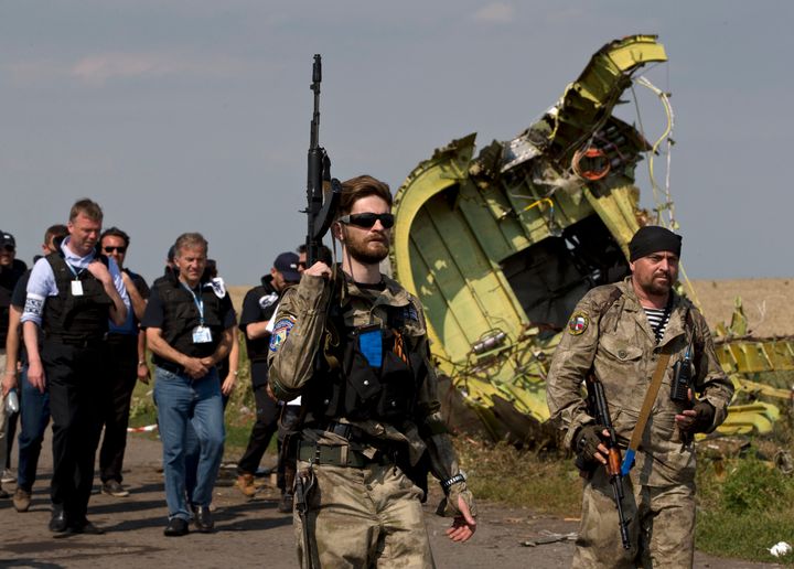 A pro-Russian rebel holds a gun passing by MH17 wreckage, five days after the crash