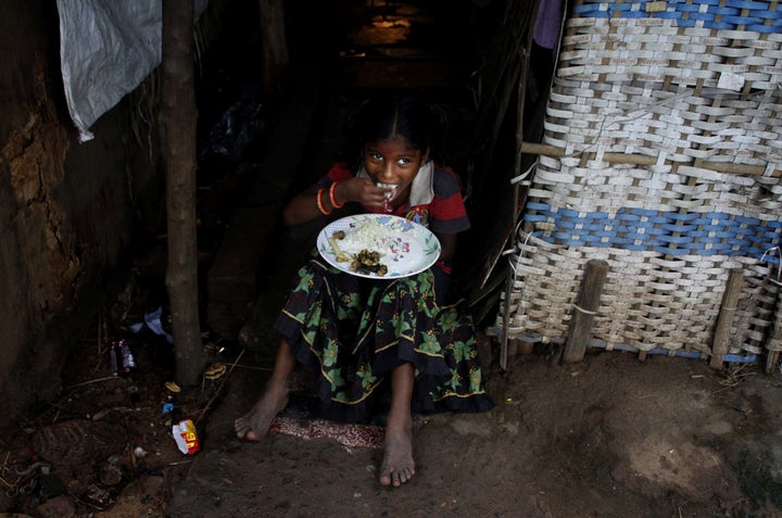 A below poverty line family girl eats food as she sits outside of her parents living makeshift at a slum in the eastern India