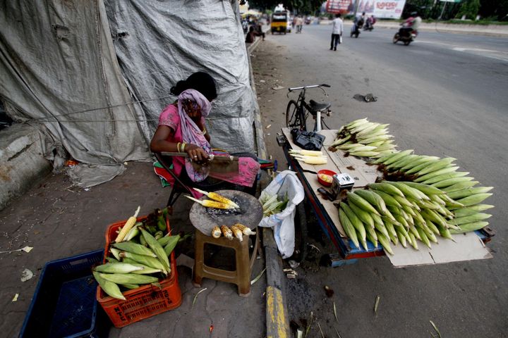A slum living girl hides herself to avoid camera as she prepares roosted corns on way side before to sale it to pedestrians in the eastern Indian city Bhubaneswar, India, Thursday, 21 July 2016.