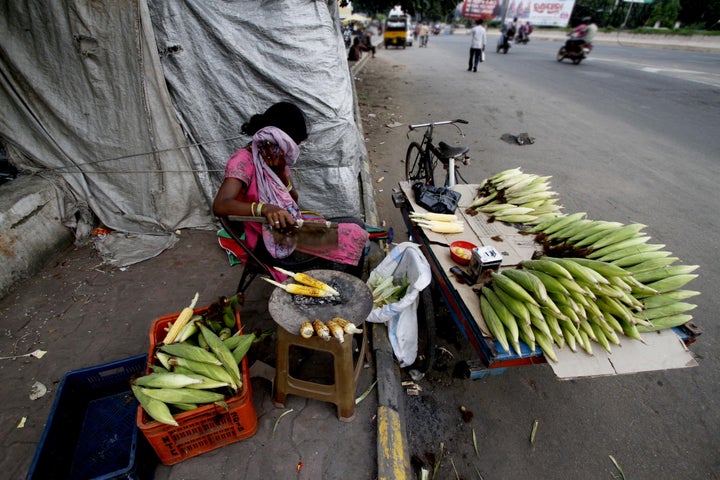 A slum living girl hides herself to avoid camera as she prepares roosted corns on way side before to sale it to pedestrians in the eastern Indian city Bhubaneswar, India, Thursday, 21 July 2016.