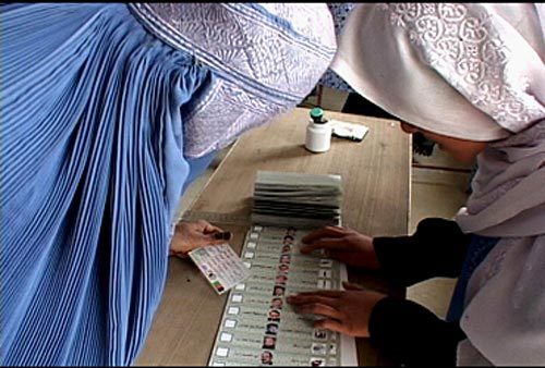 <p>Oct. 9, 2004 — A Joint Electoral Management Body employee, right, explains how to fill out an election ballot to an Afghan woman in the village of Raban during Afghanistan's first democratic presidential election October 9th.</p>