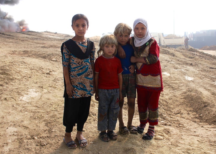 Children stand near a burning oil well, lit ablaze by ISIS in their retreat, just over a month after Iraqi forces drove out t