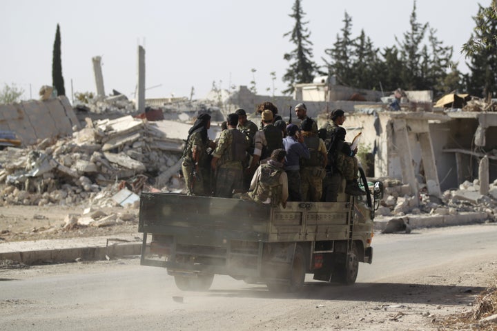 Rebel fighters drive past damaged buildings in al-Rai town, northern Aleppo countryside, Syria October 2, 2016.