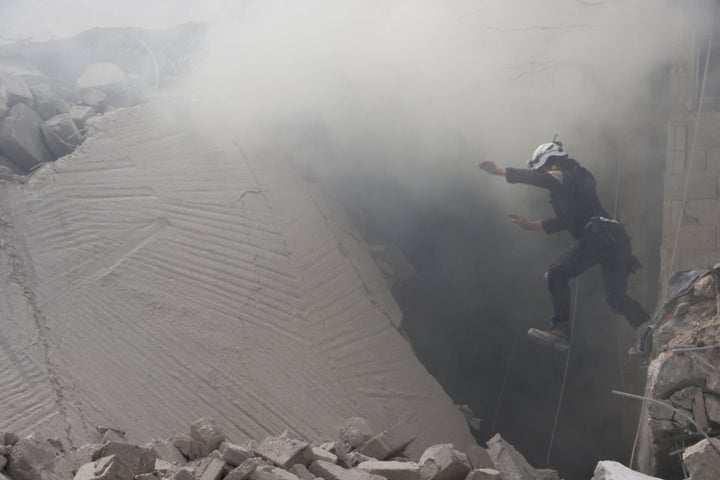 A civil defense member carries out a search and rescue operation over the wreckage of collapsed buildings in Aleppo.