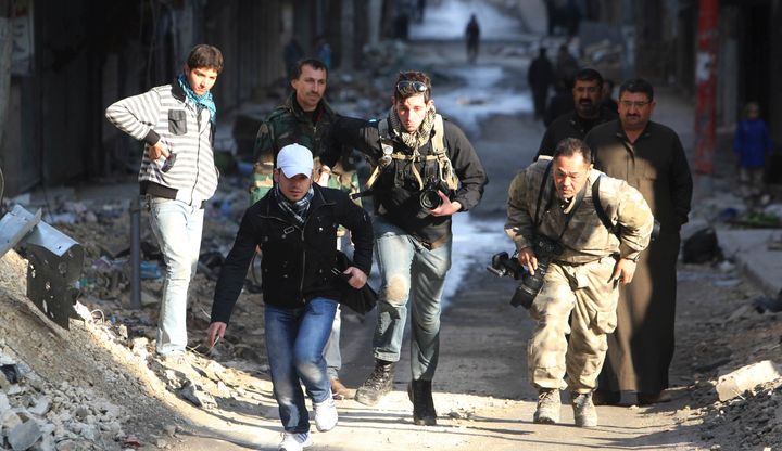 Journalists Bryn Karcha (C) of Canada and Toshifumi Fujimoto (R) of Japan run for cover next to an unidentified fixer in a street in Aleppo's district of Salaheddine December 29, 2012.