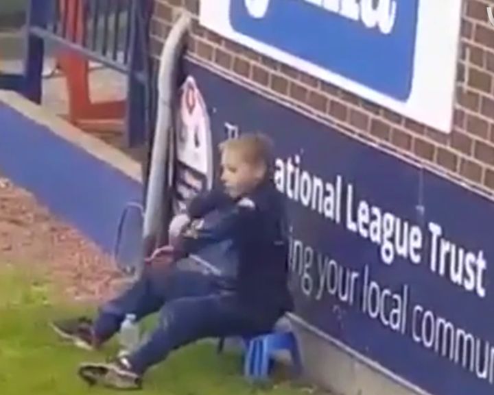 The ball boy performs a dance routine while sitting on a plastic stool during a Stockport County match
