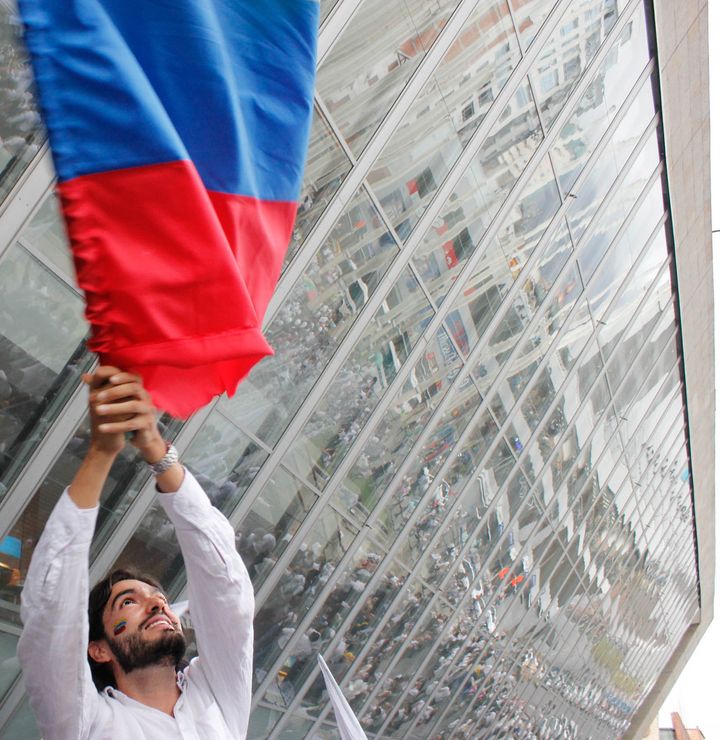 Pro-peace supporter waved a Colombian flag as thousands of marchers gathered in Medellín's Park of Lights (seen reflected in the windows of the EPM Library).