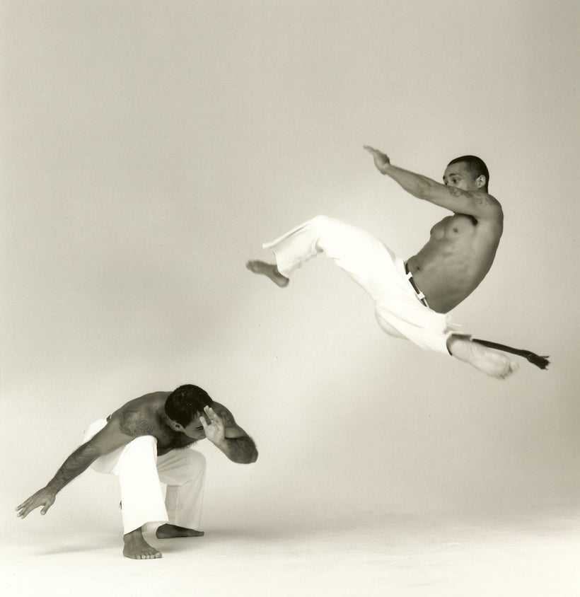 Professor Boca (right) delivering a high, fast kick called an Armada Martelo over Mestre Bom Jesus, who is in the standard Es