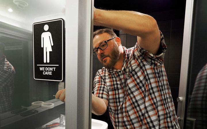 Museum manager Jeff Bell adheres informative backing to gender neutral signs in the 21C Museum Hotel public restrooms on May 10, 2016 in Durham, North Carolina.