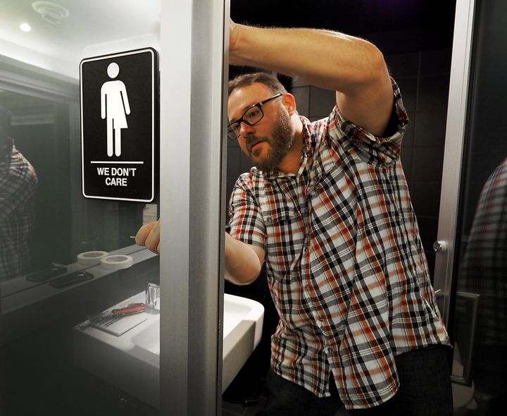 Museum manager Jeff Bell adheres informative backing to gender neutral signs in the 21C Museum Hotel public restrooms on May 10, 2016 in Durham, North Carolina.