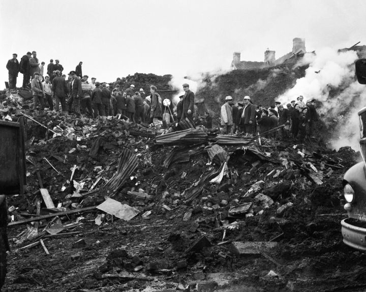 Rescue workers stand on the rubble which slid down the hill into the village of Aberfan on 21st October 1966