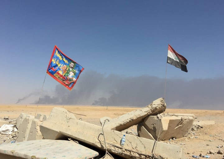 A Shiite militia flag flies next to the Iraqi flag next to Qayyarah Airfield West, where hundreds of U.S. troops are based le