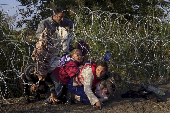 Syrian migrants cross under a fence as they enter Hungary at the border with Serbia on Aug. 27, 2015.