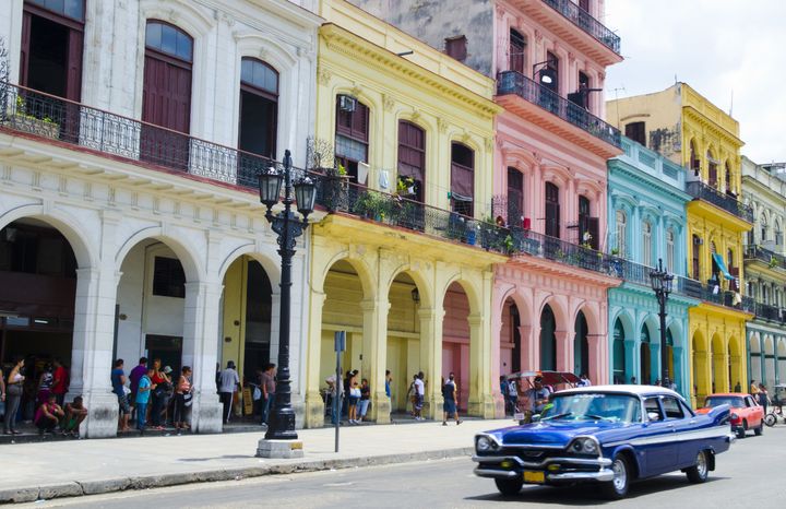 A car passes by pastel-colored buildings in Havana, Cuba.