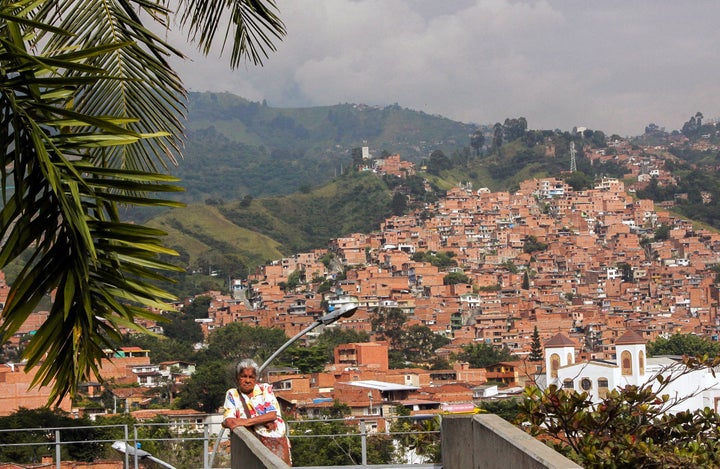 A member of the victims' rights group Women Walking for Truth waits outside of the San Javier library and community center with the neighborhood of Comuna 13 behind her.