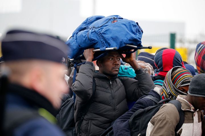 <strong>French police stand near as migrants with their belongings queue in Calais on Monday</strong>