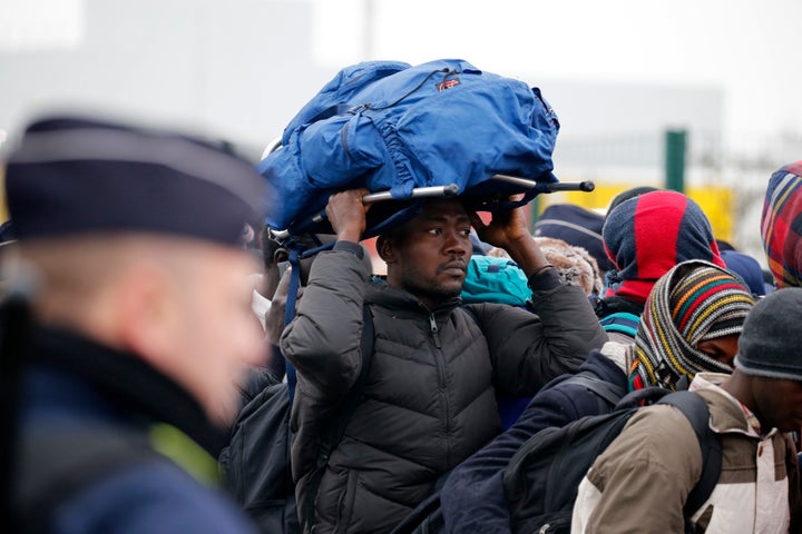 French police stand near as migrants with their belongings queue in Calais on Monday