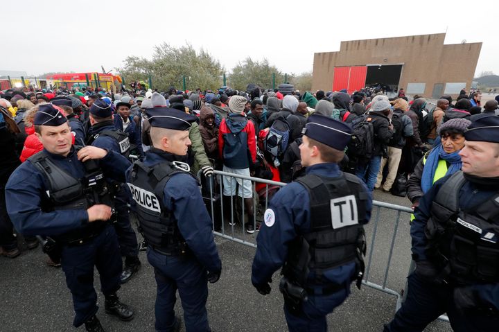 Police stand near as migrants with their belongings queue near barriers at the start of their evacuation