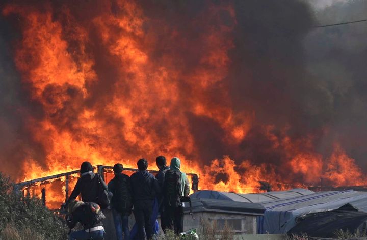 People watch as thick smoke and flames rise from amidst the tents in Calais on Wednesday