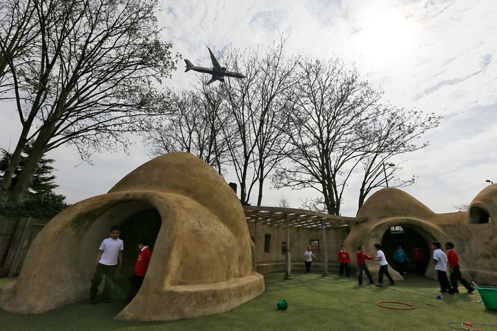 Students from Hounslow Heath Infants School play around one of four adobe huts designed to help minimise the noise of aircraft landing at Heathrow