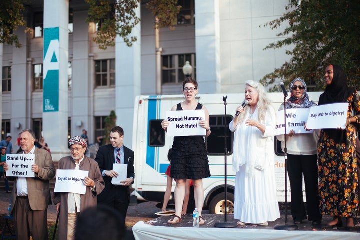 <p>Andra Baylus, center-right, leads the Spread Hummus not Hate tour delegation and rally attendees in the singing of “Peace, Salaam, Shalom”, a song meant to celebrate interfaith harmony. The Spread Hummus not Hate tour stopped at several mosques, synagogues and public venues before completing its tour at American University in a marquis rally. </p>