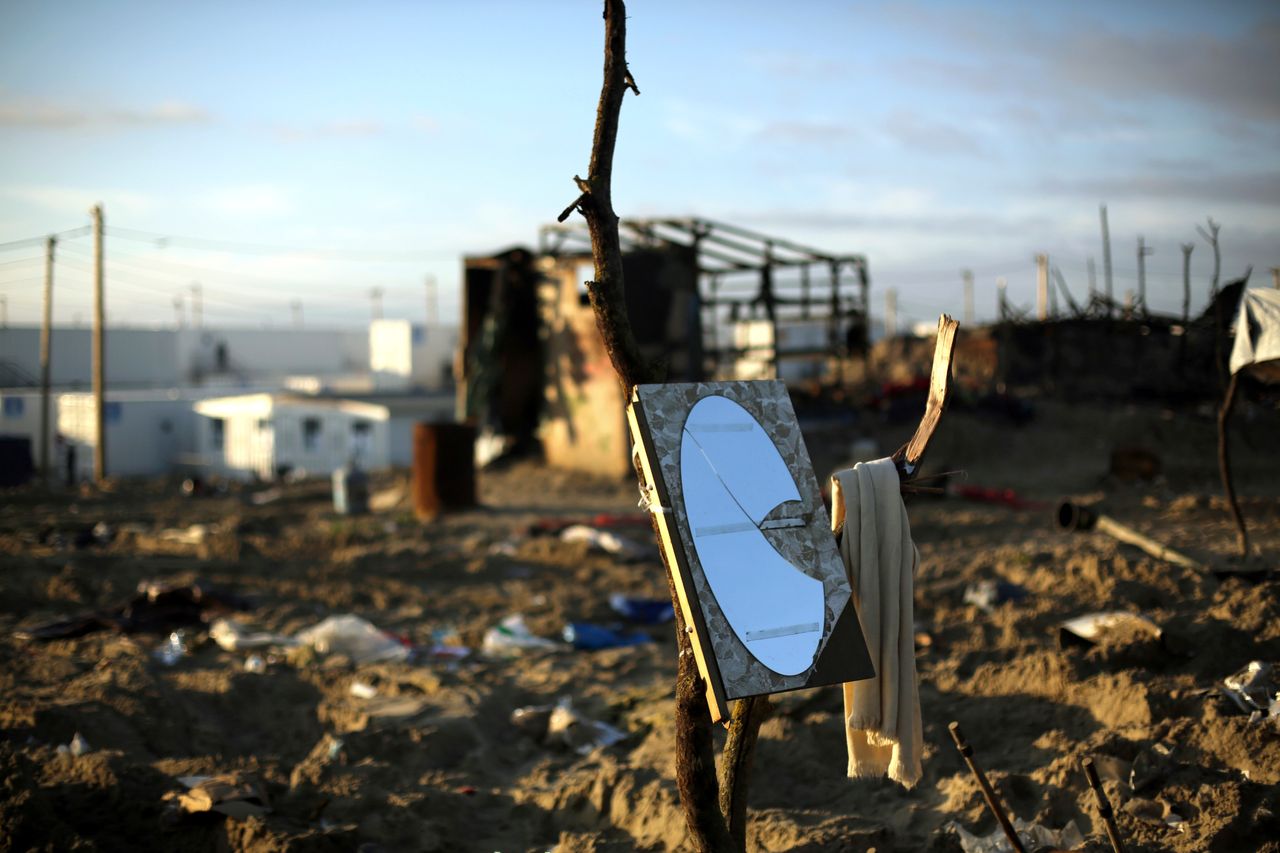 A mirror and a towel are hanging on a branch in the makeshift migrant camp.