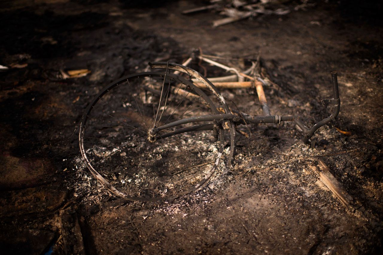 A burnt bicycle remains on the floor of a charred tent.