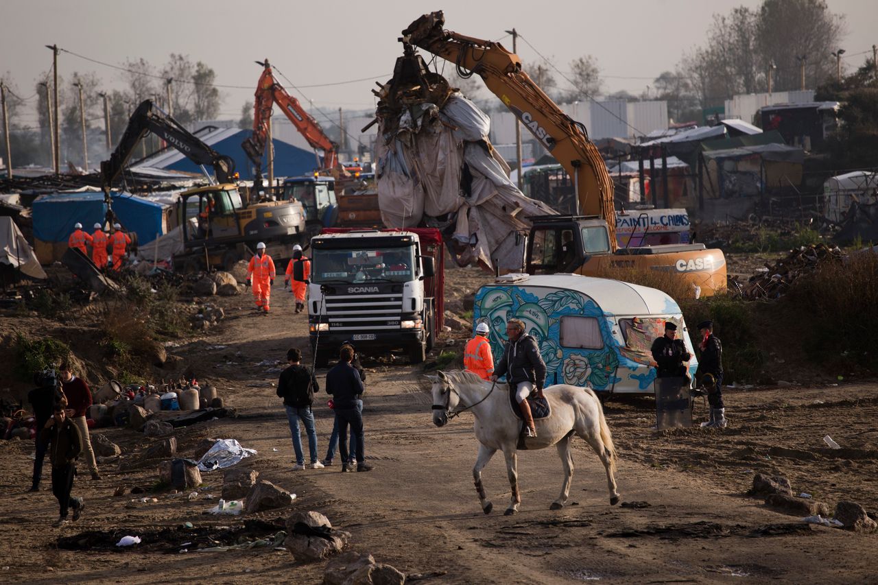 A man rides a horse past mechanical diggers working to clean up a makeshift migrant camp.