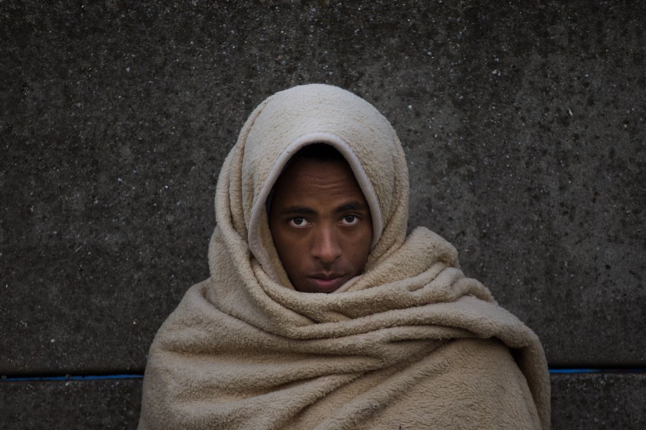 Abdelhamid, 17, from Eritrea, waits with a group of other migrants with nowhere to go, in the hope an official bus will come to take them away to be processed after being forced out from the makeshift migrant camp.