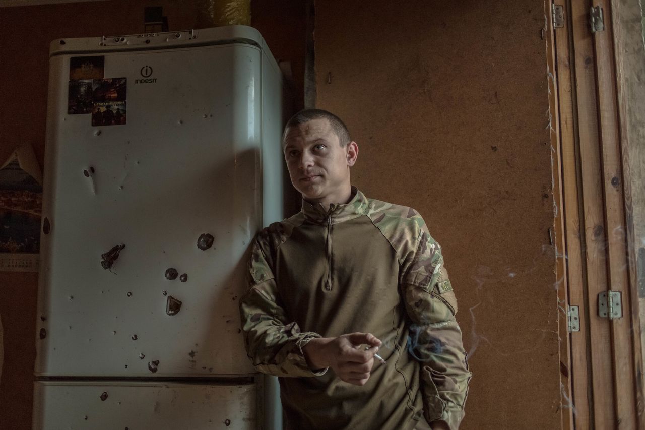 A volunteer soldier stands next to a bullet-ridden fridge. He says he joined the unit because he just wanted to fight.