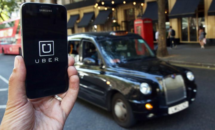 The Uber logo is seen on a smartphone while a British taxi waits in the background in this 2016 file photo.