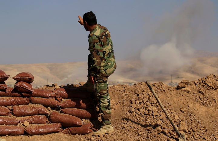 A Kurdish Peshmerga soldier who is stationed between two front lines gestures as a smoke rises near Bashiqa, east of Mosul, I