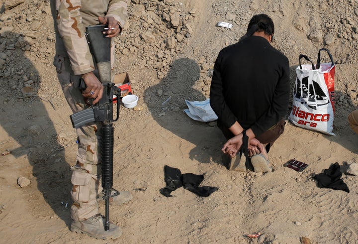 An Iraqi soldier stands next to a detained man, accused of being an Islamic State fighter, at a check point in Qayyarah, sout