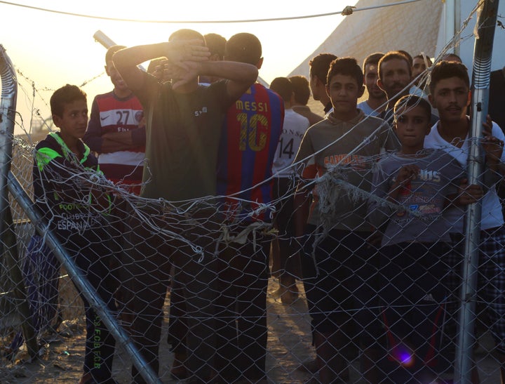 Iraqi men and boys stand inside of a fenced-in area next to a screening center at Debaga camp. Some are detained there f