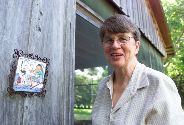 Janet Reno smiles as she greets the media next to a caricature of a journalist and fisherman at the back entrance to her home