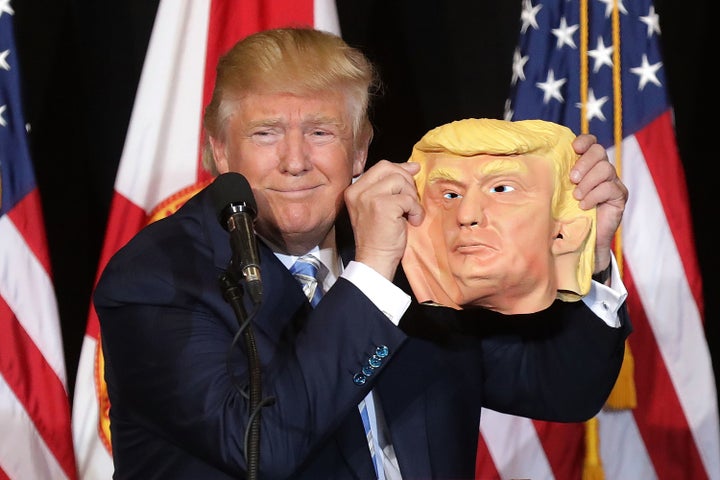 Republican presidential nominee Donald Trump holds up a rubber mask of himself during a campaign rally in the Robarts Arena a