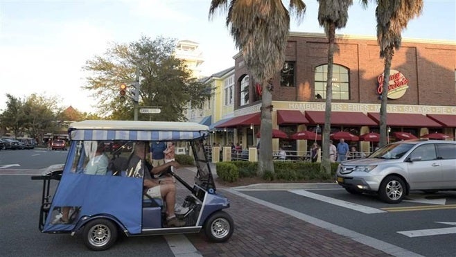 Residents ride their golf cart on a street at the Lake Sumter Landing Market Square in The Villages, Florida. Growing numbers