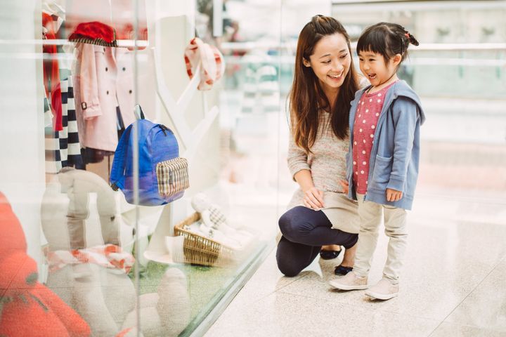 Pretty young mom and lovely little daughter looking at window display for kids wears in a shopping mall joyfully. Images By Tang Ming Tung via Getty Images