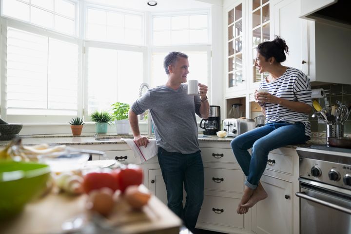 Couple drinking coffee talking in kitchen Hero Images via Getty Images