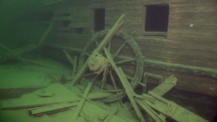 The helm wheel is seen leaning against the wreck's starboard side.