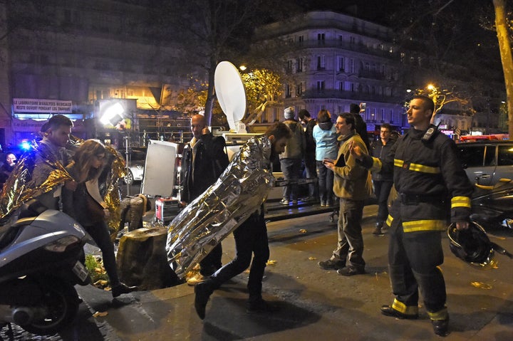 People wearing survival blankets walk by a rescuer near the Bataclan concert hall in central Paris, early on Nov.14, 2015.