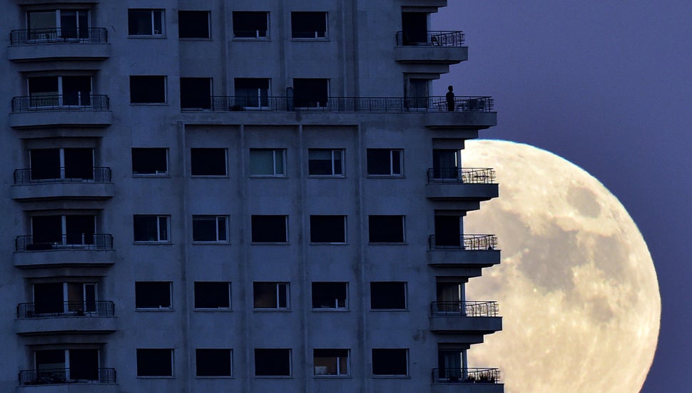 A man stands on a balcony in Madrid on Sunday, the eve of a "supermoon," as the moon rises in background.