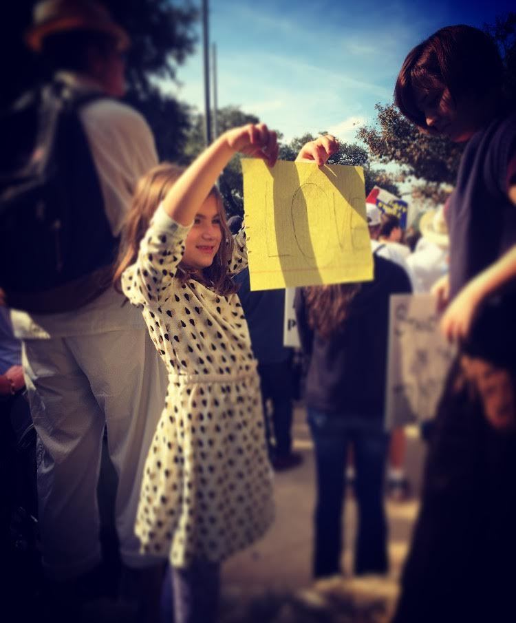 Daughter holding up a sign at a peaceful gathering in Austin.