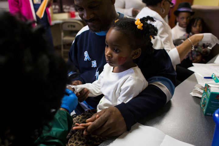 Azariah Hawthorne, 2, is held by her grandfather Nile Hawthorne Sr., 46, as she gets her blood lead levels tested at Carriage Town Ministries in Flint in February.