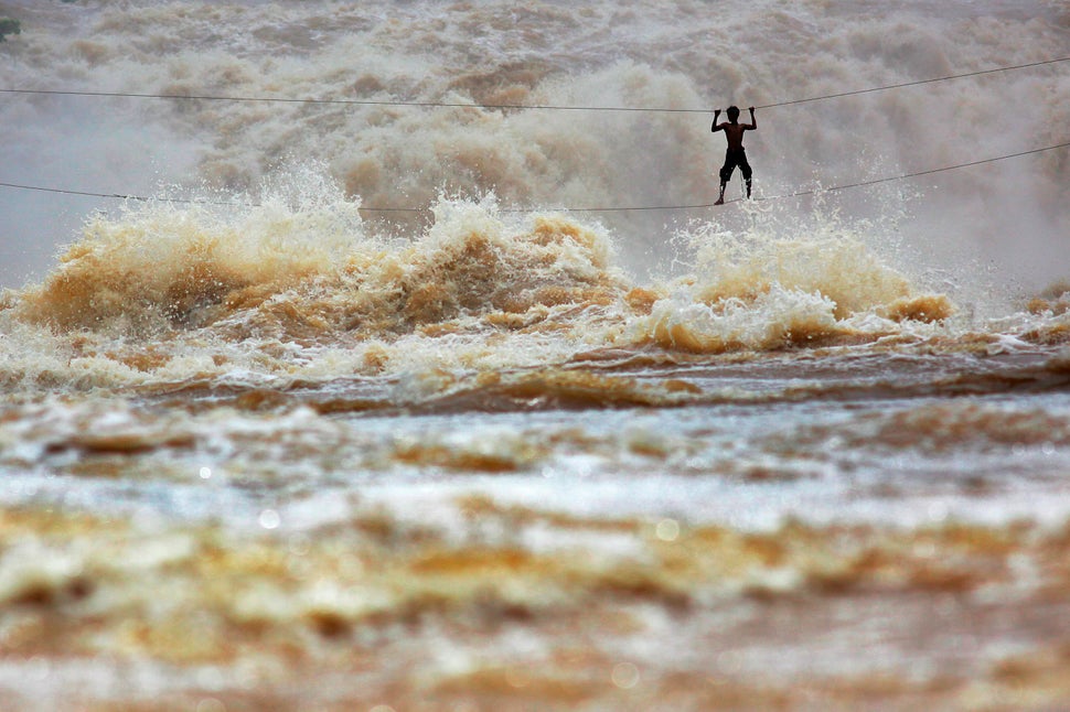 During the rainy season, huge waves dwarf Laotian fisherman Samnieng as he uses a homemade high-wire bridge to cross over the