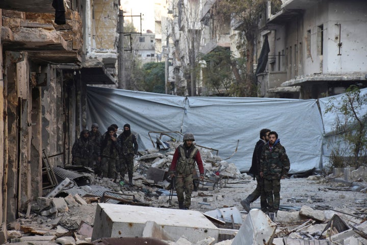 Syrian government soldiers walk amid rubble of damaged buildings, near a cloth used as a cover from snipers, after they took