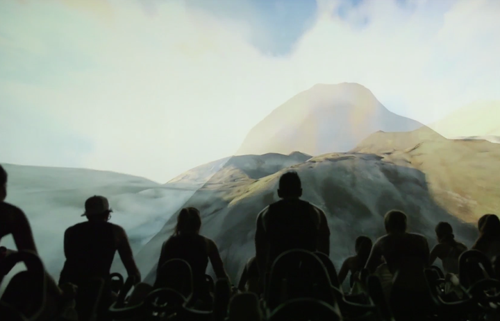 Cyclers during an IMAX Shift watch moving images of mountains.