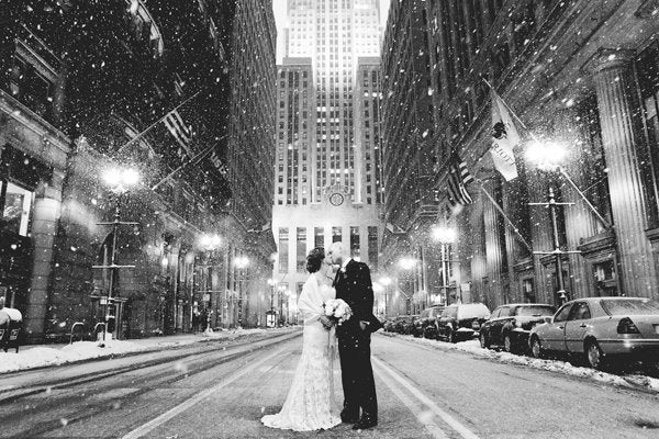 A black and white still of a city getting sprinkled in snow as bride and groom share a kiss is nothing but glamorous.