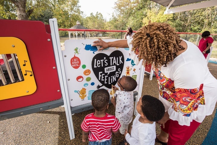 Young children examine a literacy panel similar to the ones at Officer Willie Wilkins Park in Oakland, California.